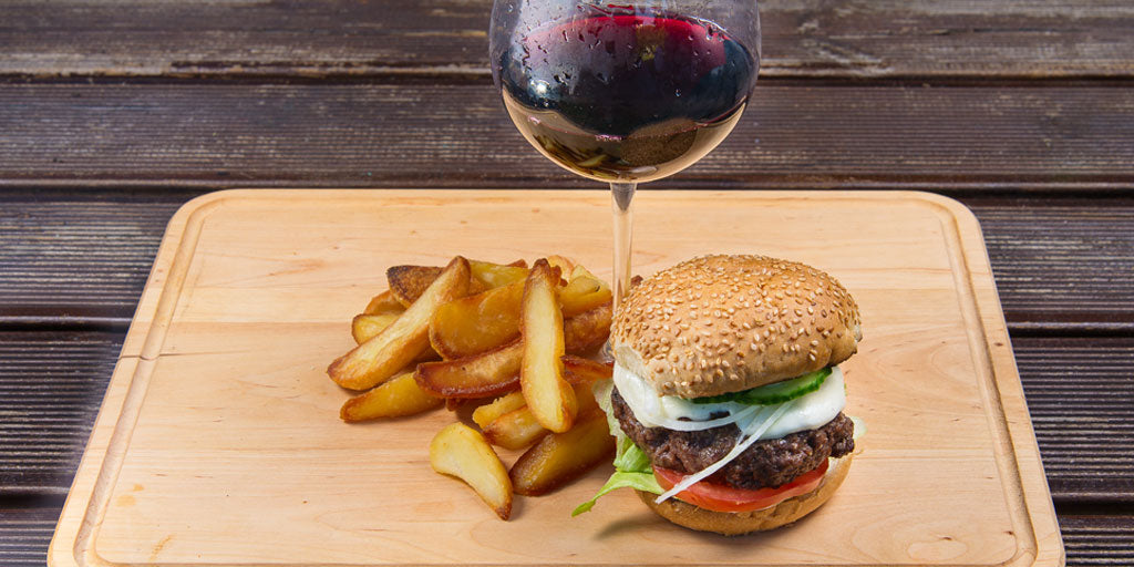 Glass of wine with burger and fries on wooden board