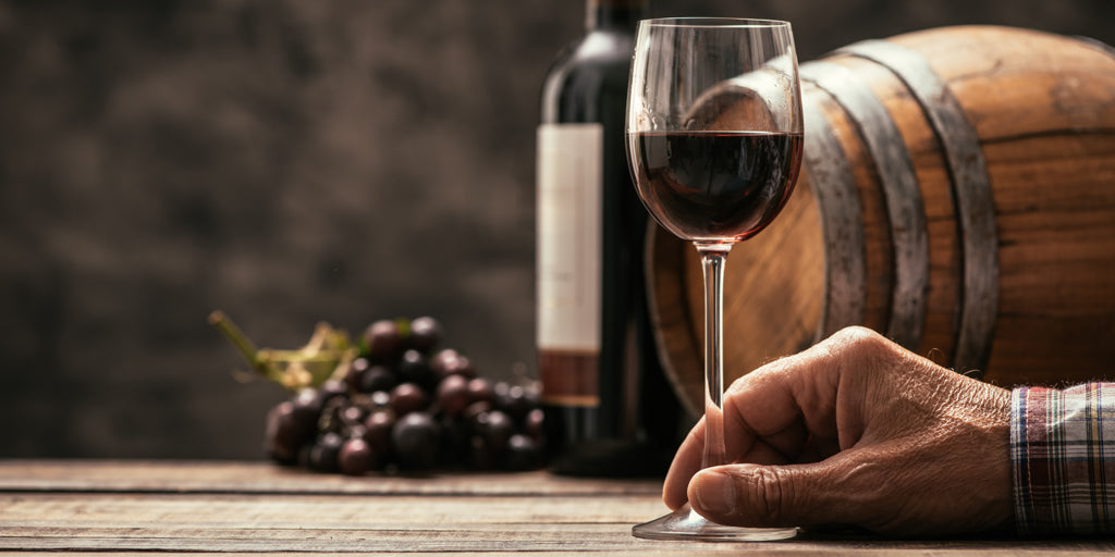 man's hand with wine glass, grapes and barrel