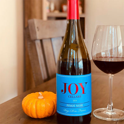 A bottle and glass of Joy Cellars 2018 Pinot Noir next to a mini pumpkin on a wooden table