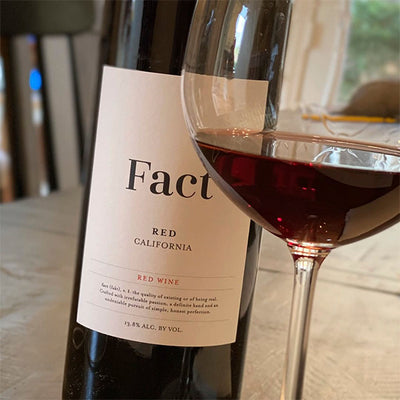 A close up image of Fact Red Wine alongside a filled glass on a dining room table