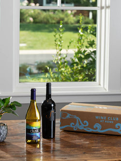 1 dry white and 1 dry red WineShop At Home artisan wines for Wine Club Membership displayed on kitchen table with the Wine Club box.