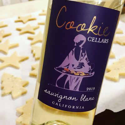 A close up of a bottle of Cookie Cellars 2019 Sauvignon Blanc in front of some Christmas themed pre-baked cookies