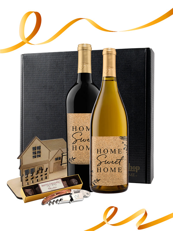 Two bottles of wine with 'Home Sweet Home' labels, a chocolate bar, and a bottle opener in front of a black gift box.