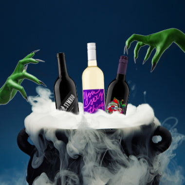 Three wine bottles arranged on a white cauldron with dramatic smoke against a dark blue background, with green zombie hands reaching in from both sides. The center bottle has a white label reading 'You Sexy Thing' in purple script.